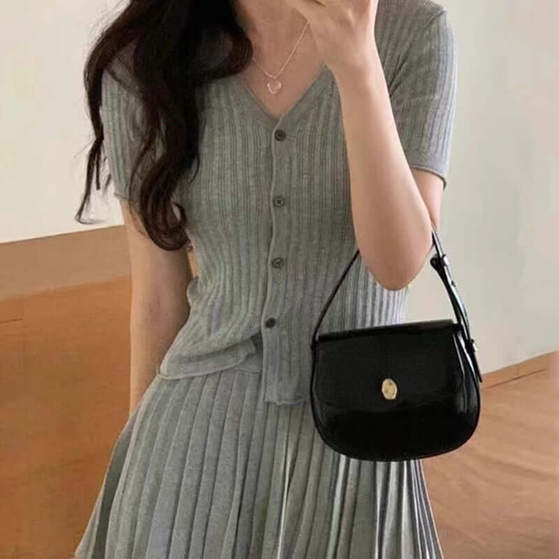 Casual outfit featuring a soft grey ribbed top and pleated skirt, complemented by a stylish black handbag.