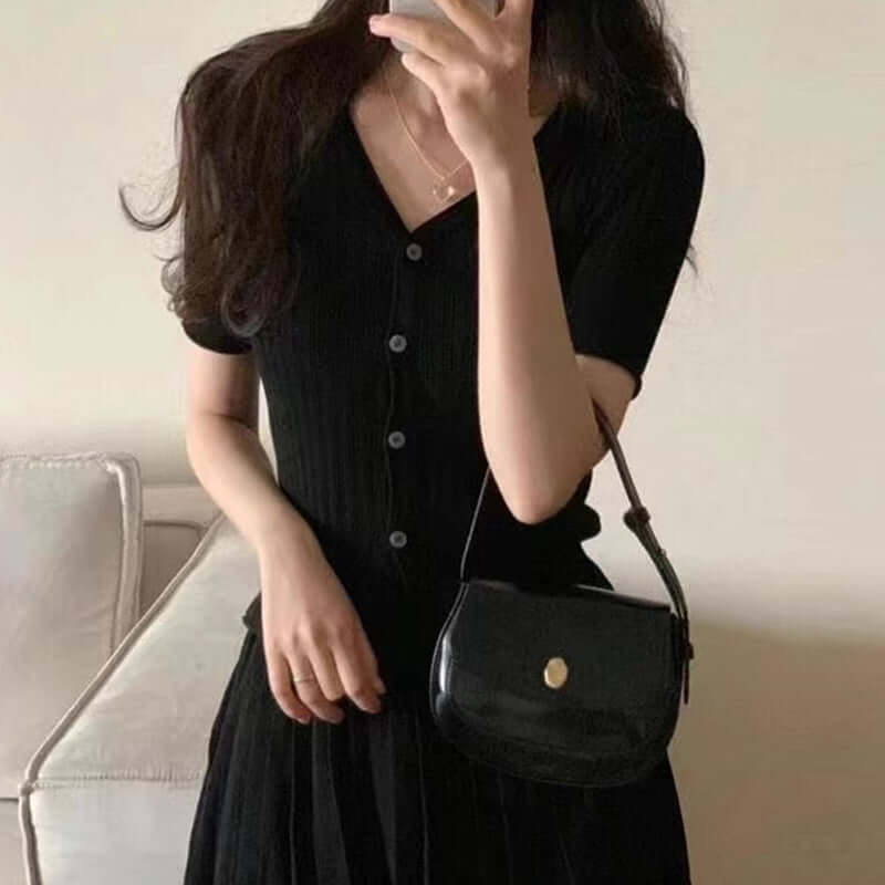 Elegant black pleated dress with a v-neckline, complemented by a stylish mini handbag.