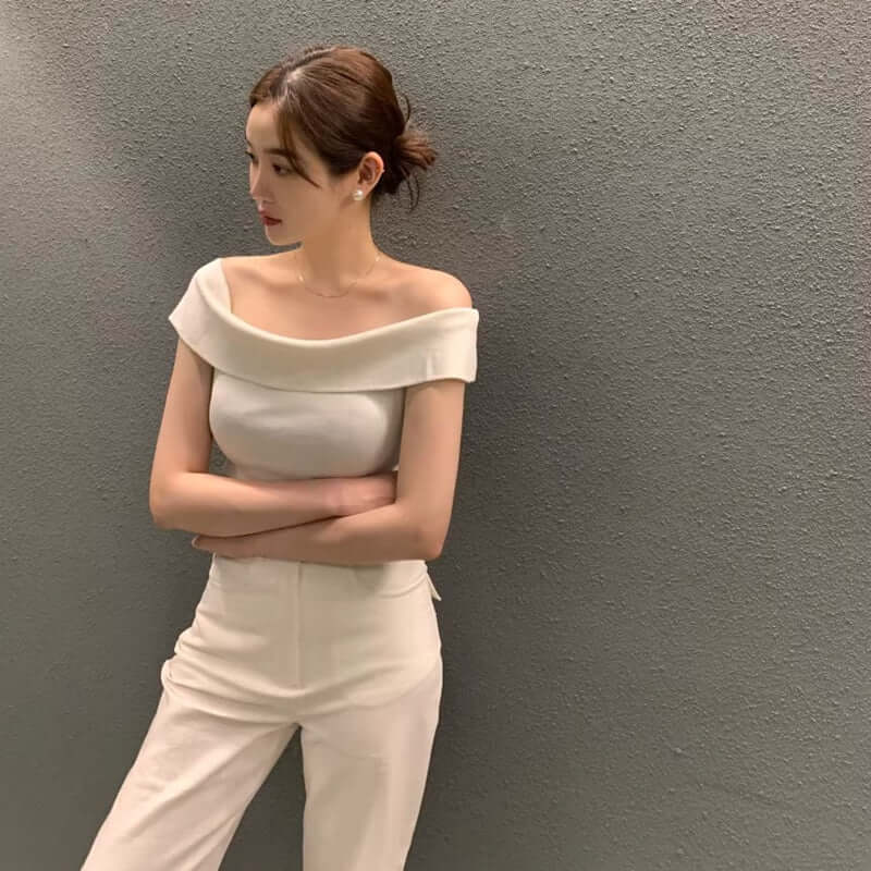Elegant off-shoulder top with a wide collar, paired with stylish white pants, showcasing a chic and modern look.